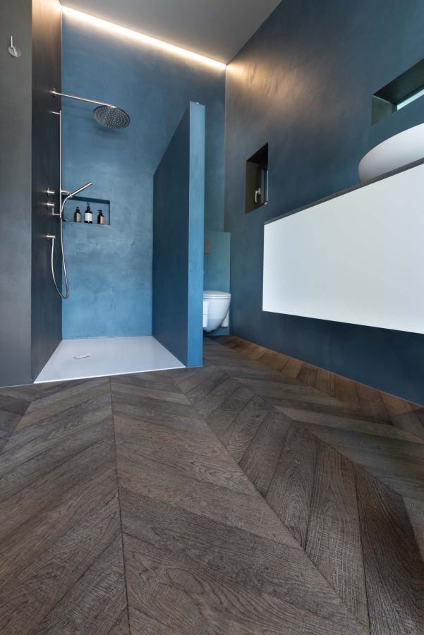 Badezimmer: blaue gestrichene Wände, Regenwalddusche und grau-brauner Parkett im Fischgratmuster, sägeroh.